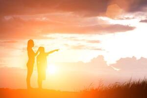 Silhouette Mutter und Sohn bei Sonnenuntergang, zeigt auf die Sonne foto