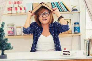 Schöne Hipster-Frau bedeckt ihren Kopf mit einem Buch und hat Angst, dass etwas herunterfällt foto