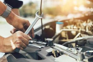 Der Automechaniker hält einen Schraubenschlüssel bereit, um den Motor und die Wartung zu überprüfen. foto