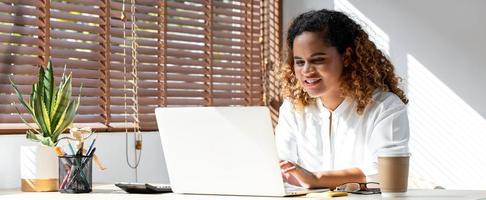 banneraufnahme einer glücklichen jungen afroamerikanischen geschäftsfrau, die von zu hause aus auf einem laptop im wohnzimmer arbeitet foto