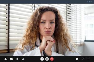 ernsthafte Ärztin, die aufmerksam zuhört und die Hände unter dem Kinn hält, während sie einen Videoanruf für medizinische Konferenzen aus dem Krankenhaus tätigt foto