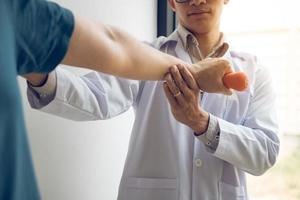 asiatischer junger männlicher physiotherapeut, der patienten beim heben von hanteln hilft, übungen im büro. foto