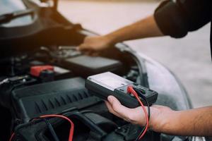 Der Automechaniker trägt ein Batteriemessgerät und überprüft den allgemeinen Zustand des Motors. foto