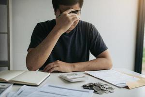 asiatische Männer sind wegen finanzieller Probleme gestresst, mit Rechnungen und Taschenrechnern, die auf den Tisch gelegt werden, während sie Probleme mit Haushaltsausgaben haben. foto