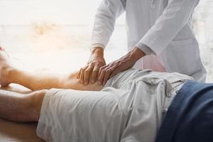 Physiotherapeuten verwenden die Hände, um den Oberschenkel des Patienten zu greifen, um in der Klinik auf Schmerzen und Massagen zu prüfen.