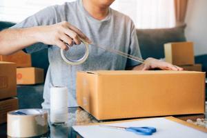 Teenager aus asiatischen Unternehmern verwenden das Klebeband, um die Schachtel zu versiegeln, indem sie das Produkt verpacken, um es an die Kunden zu senden. foto