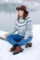 Frau sitzt und meditiert in der Yoga-Pose auf dem Schnee vor dem Hintergrund der Winterlandschaft foto