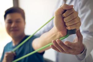 Nahaufnahme eines Handpatienten, der Dehnübungen mit einem flexiblen Übungsband und einer Hand eines Physiotherapeuten durchführt, um im Klinikraum zu helfen. foto