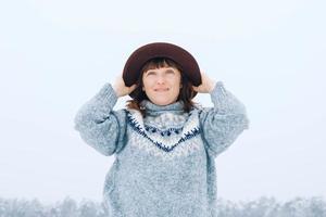 Frau mit braunem Hut und Pullover vor dem Hintergrund eines schneebedeckten Waldes foto