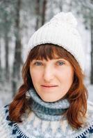 Winterporträt einer Frau in einem warmen Hut und Pullover auf dem Hintergrund eines verschneiten Waldes foto
