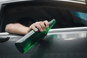 asiatischer mann, der während der fahrt eine flasche bier vor dem auto hält. foto