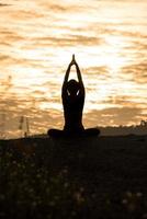 Silhouette junge Frau praktiziert Yoga auf dem Berg bei Sonnenuntergang. foto