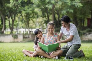 glückliche familienmutter, vater und tochter lesen ein buch im park foto