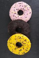 hausgemachte Donuts mit farbigem Zuckerguss auf schwarzem Hintergrund. foto