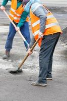 zwei straßenarbeiter schaufeln alten asphalt von der straße und laden ihn in eine planierschaufel. foto