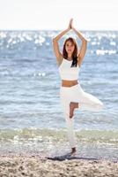 junge Frau beim Yoga am Strand in weißer Kleidung foto