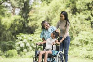 glückliche Großmutter im Rollstuhl mit ihrer Tochter und ihrem Enkel in einem Park, glückliches Leben glückliche Zeit.