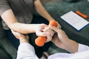 asiatische physiotherapeuten helfen patienten beim heben von hanteln durch seine rehabilitation in der klinik. foto