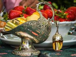 silberne Zuckerdose in Form eines Körbchens für Kohle. Antiquitäten für den Tisch. elegante reichhaltige Gerichte zum Dekorieren eines Festmahls. Erdbeeren zum Nachtisch. foto