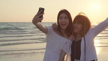 junges asiatisches lesbisches paar mit smartphone, das selfie in der nähe des strandes macht. schöne frauen lgbt paar glücklich entspannen genießen liebe moment wenn sonnenuntergang am abend. Lebensstil lesbisches Paar reist am Strandkonzept foto