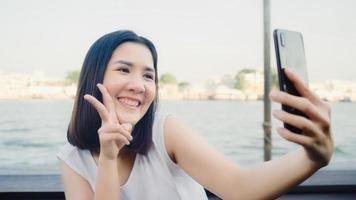 reisende asiatische bloggerin, die selfie mit handy im café anklickt, schöne frau mit smartphone macht vlog und lebt in sozialen medien, während sie die reise genießt urlaubsreise in der nähe des flusses in der stadt. foto