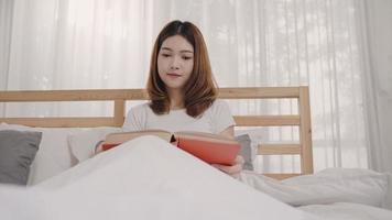 schöne attraktive junge asiatische frau, die ein buch liest, während sie auf dem bett liegt, wenn sie sich morgens in ihrem schlafzimmer zu hause entspannt. Lifestyle-Frauen mit Entspannungszeit zu Hause Konzept. foto