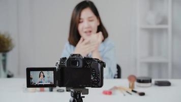 glücklich lächelnde asiatische Frau oder Schönheitsblogger mit Pinsel und Kamera, die Video aufzeichnen und Hand zu Hause winken. Schönheit Videoblog Blogging Menschen Konzept. foto