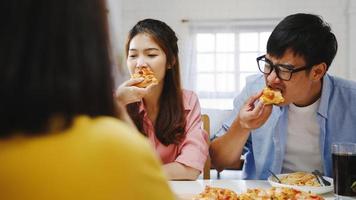 glückliche Gruppe junger Freunde, die zu Hause zu Mittag essen. asien-familienfeier, die pizza essen isst und lacht, mahlzeit genießt, während sie zusammen am esstisch im haus sitzt. feier urlaub und zusammengehörigkeit. foto