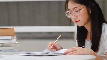 asiatische studentinnen, die bücher in der bibliothek der universität lesen. junge Studentin macht Hausaufgaben, liest Lehrbuch, lernt hart für Wissen und Bildung am Hörpult auf dem College-Campus. foto