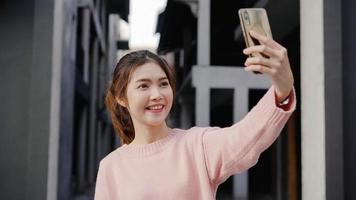 Fröhliche, schöne junge asiatische Backpacker-Bloggerin mit Smartphone, die ein Selfie macht, während sie in Chinatown in Peking, China, unterwegs ist. Lifestyle-Rucksack touristisches Reise-Urlaubskonzept. foto