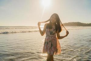 junge asiatische frau, die sich am strand glücklich fühlt, schöne weibliche glückliche entspannen lächelnden spaß am strand in der nähe des meeres bei sonnenuntergang am abend. Lifestyle-Frauen reisen am Strandkonzept. foto