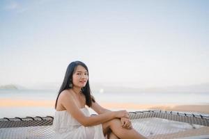 junge asiatische frau, die auf hängematte sitzt, entspannen sich am strand, schöne weibliche glückliche entspannen sich nahe meer. Lifestyle-Frauen reisen am Strandkonzept. foto