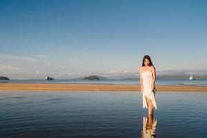 junge asiatische Frau, die am Strand geht. schöne Frau glücklich entspannen am Strand nahe Meer, wenn Sonnenuntergang am Abend. Lebensstil Frauen reisen am Strand Konzept. foto