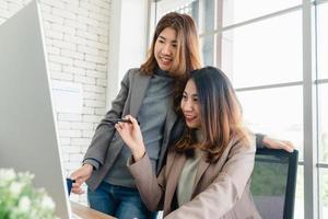 Zwei junge asiatische Geschäftsfrauen, die im Büro eines kleinen Unternehmens zusammenarbeiten und einen Bericht oder Papierkram mit erfreutem Lächeln und erfolgreicher Teamarbeit lesen. Geschäfts-, Technologie- und Bürokonzept. foto