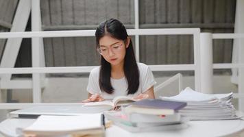 asiatische studentinnen, die bücher in der bibliothek der universität lesen. junge Studentin macht Hausaufgaben, liest Lehrbuch, lernt hart für Wissen und Bildung am Hörpult auf dem College-Campus. foto