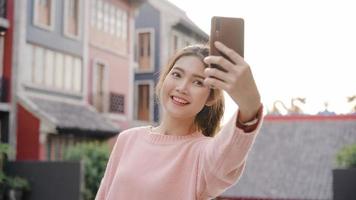 Fröhliche, schöne junge asiatische Backpacker-Bloggerin mit Smartphone, die ein Selfie macht, während sie in Chinatown in Peking, China, unterwegs ist. Lifestyle-Rucksack touristisches Reise-Urlaubskonzept. foto