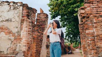 reisende asiatische frau, die kamera verwendet, um ein foto zu machen, während sie ihre urlaubsreise in ayutthaya, thailand, verbringt, japanische touristin genießt ihre reise zu einem erstaunlichen wahrzeichen in einer traditionellen stadt.