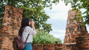 reisende asiatische frau, die kamera verwendet, um ein foto zu machen, während sie ihre urlaubsreise in ayutthaya, thailand, verbringt, japanische touristin genießt ihre reise zu einem erstaunlichen wahrzeichen in einer traditionellen stadt.