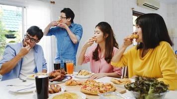 glückliche Gruppe junger Freunde, die zu Hause zu Mittag essen. asien-familienfeier, die pizza essen isst und lacht, mahlzeit genießt, während sie zusammen am esstisch im haus sitzt. feier urlaub und zusammengehörigkeit. foto