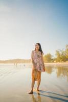 junge asiatische frau, die sich am strand glücklich fühlt, schöne weibliche glückliche entspannen lächelnden spaß am strand in der nähe des meeres bei sonnenuntergang am abend. Lifestyle-Frauen reisen am Strandkonzept. foto