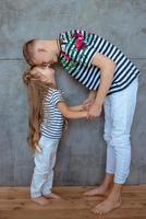 Stilvolle kaukasische Geschwister in gestreiften T-Shirts und weißen Hosen, die im Loft-Interieur stehen. Familien-, Mode-, Verwandten-, Beziehungs- und Kinderkonzept. foto