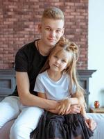 kaukasische geschwister - teenagerjungenbruder und kleine mädchenschwester, die auf einer couch im modernen loftinnenraum sitzen foto