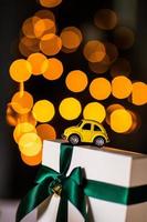 gelbes kleines Retro-Spielzeugauto auf weißem Geschenk mit grünem Band auf einem weihnachtlichen gelben Bokeh-Hintergrund. Lieferung. neujahr, weihnachten, valentinstag, weltfrauentag, verkaufskonzept. foto