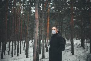 ein junger mann mit kurzen haaren in einer medizinischen maske geht im wald spazieren. foto