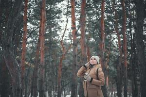 Ein junges Mädchen in Winterkleidung und eine Tasse heißes Getränk geht im Wald spazieren. foto