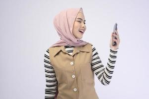 Portrait der schönen Frau mit Hijab mit Handy auf weißem Hintergrund foto