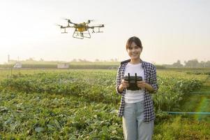 Junger intelligenter Landwirt, der Drohnen kontrolliert, die Düngemittel und Pestizide über Ackerland sprühen, hochtechnologische Innovationen und intelligente Landwirtschaft foto