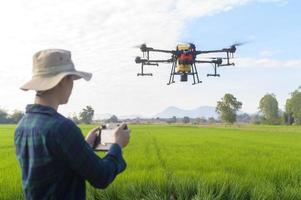 Junger intelligenter Landwirt, der Drohnen kontrolliert, die Düngemittel und Pestizide über Ackerland sprühen, hochtechnologische Innovationen und intelligente Landwirtschaft foto