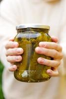 Frau Hausfrau Hand hält Glas mit eingelegten Gurken. Hauszubereitung Einlegen und Einmachen von Gemüse, Winter Bio-Lebensmittel. gesunde fermentierte hausgemachte marinierte gurken im glas. foto