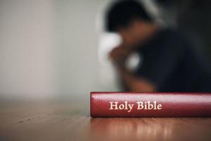 mann mit betender bibel, hände zusammengefaltet auf ihrer bibel auf holztisch. foto